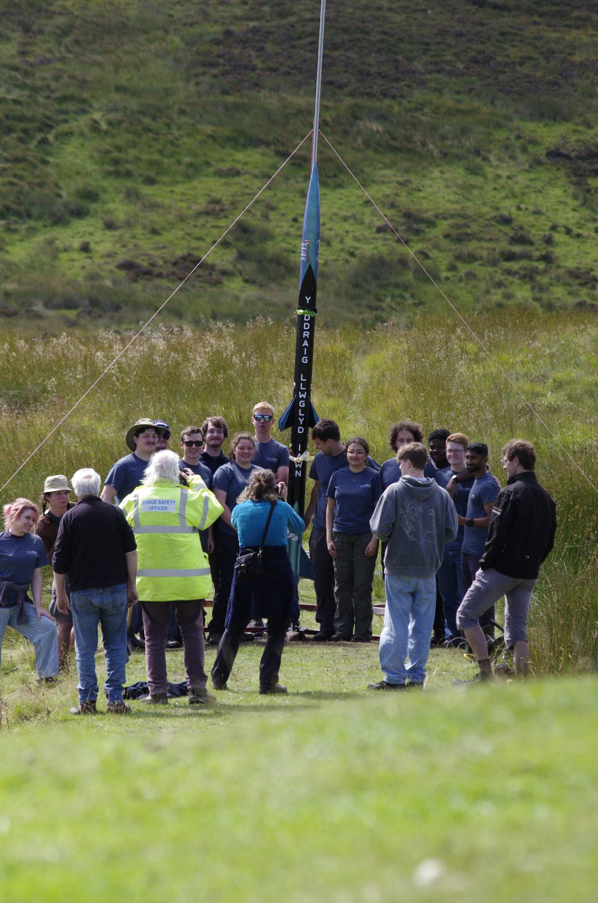 A university rocketry team gathered beside a large rocket at the 2026 event